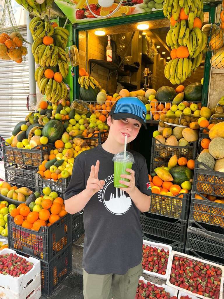 Child drinking lemon mint juice with food in the background on Amman Food Tours